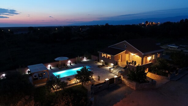 Una casa grande con piscina, mobiliario exterior y un patio bien iluminado.