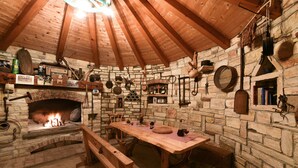 Una habitación rústica con paredes de piedra, una mesa de madera, bancos y una chimenea.