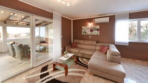 Una sala de estar con un ventanal corredizo que da a un balcón, un sofá color beige, una mesa de centro de vidrio y un cuadro en la pared.