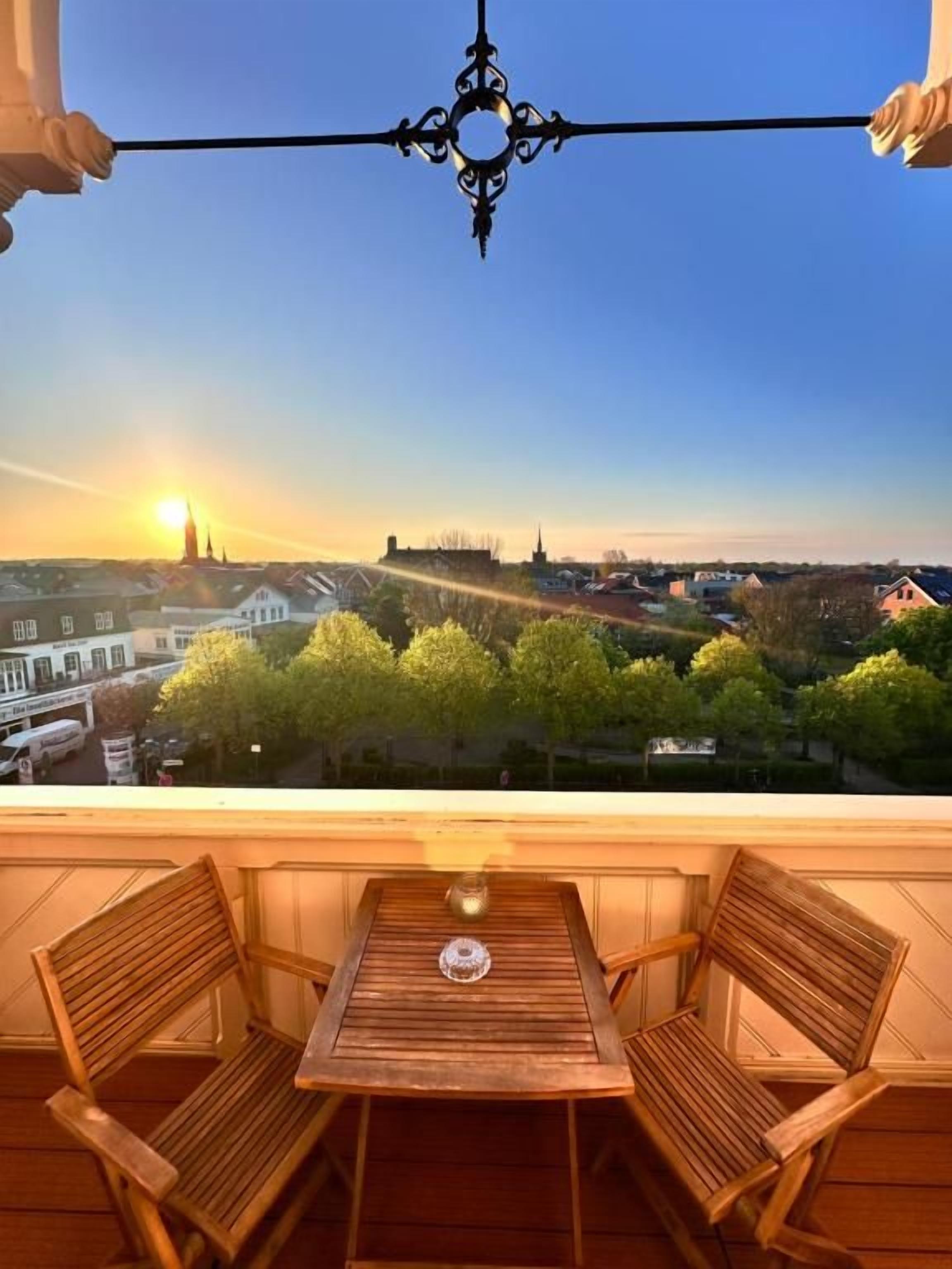 Ein Balkon mit Tisch und Stühlen, mit Blick auf eine Stadtlandschaft aus Gebäuden und Bäumen.