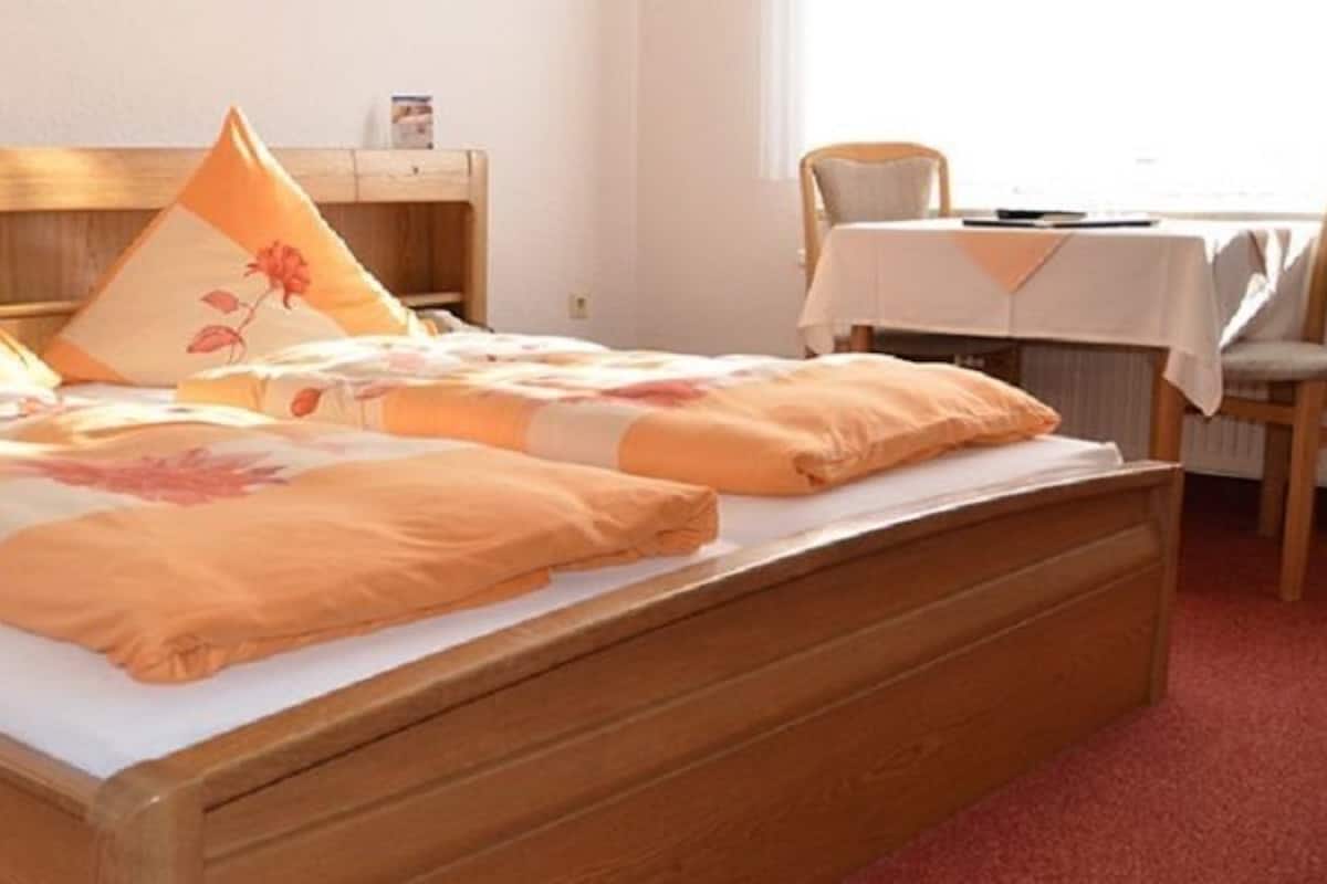A double bed with floral bedding, a wooden headboard, and a bedside table.