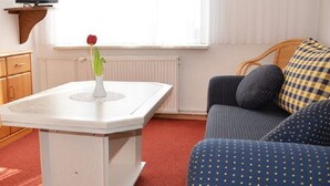 Et værelse med et hvidt bord, et træskab, en blå sofa og et vindue med persienner.