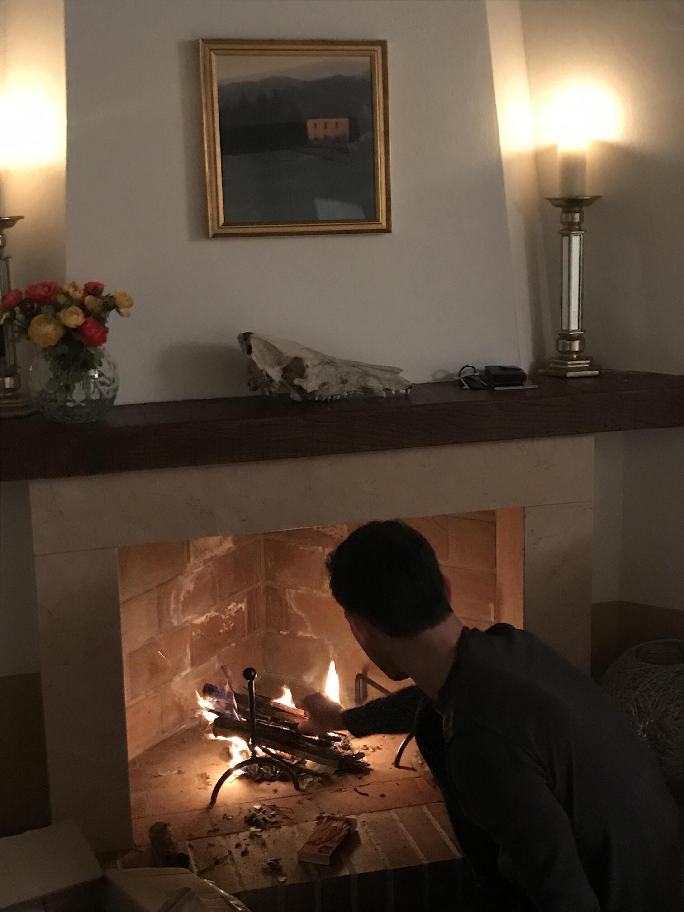Una llar de foc encès, un quadre emmarcat a sobre i un vas amb flors al mantell.