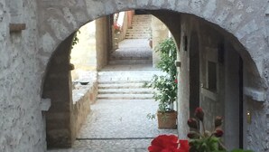 Eine steinerne Treppe führt zu einem Gebäudeeingang, der von einem Bogen mit roten Blumen im Vordergrund gerahmt wird.
