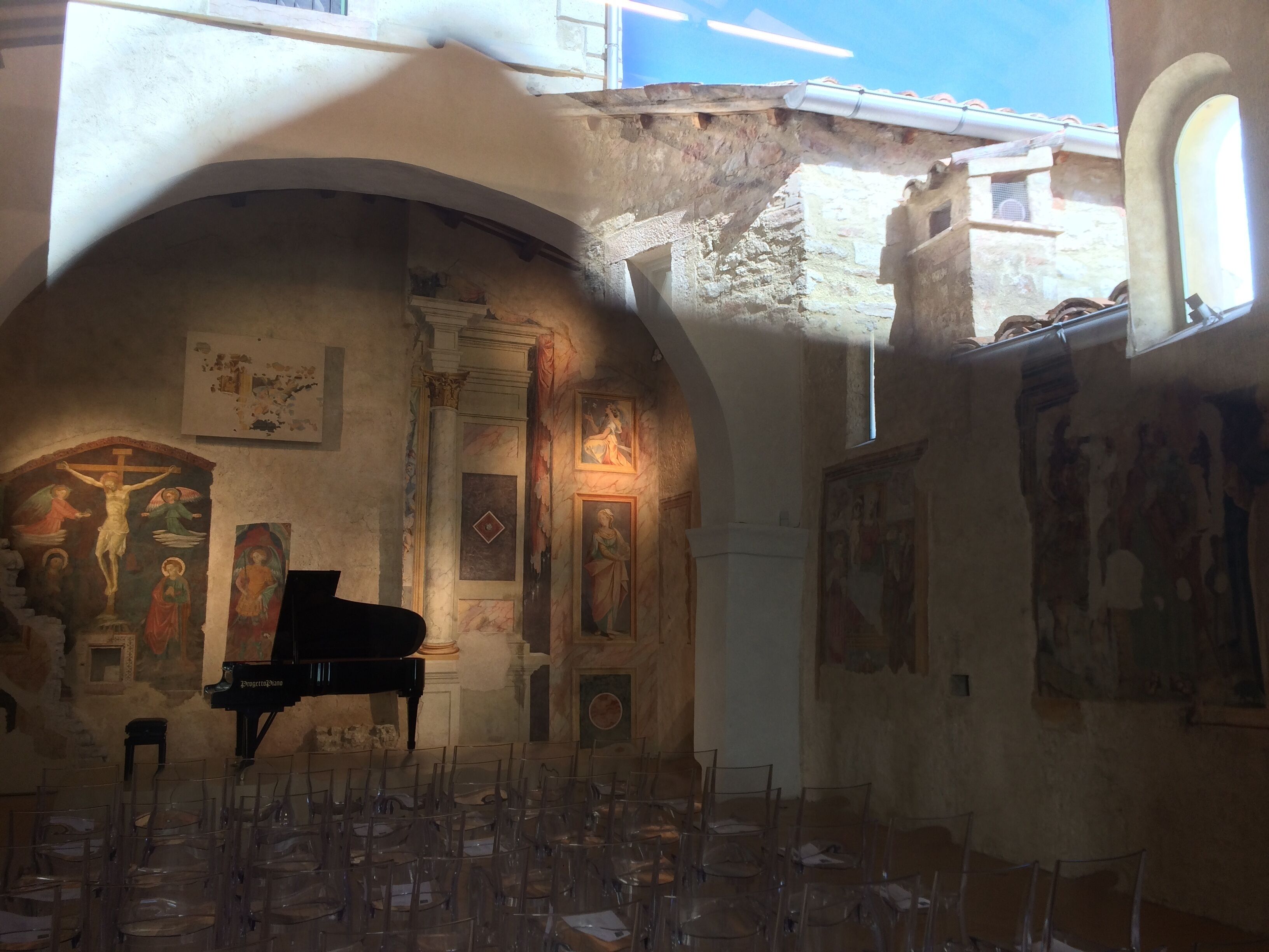 L’intérieur d’une église, avec un grand piano, des chaises en verre transparent et des œuvres d’art religieux accrochées aux murs.