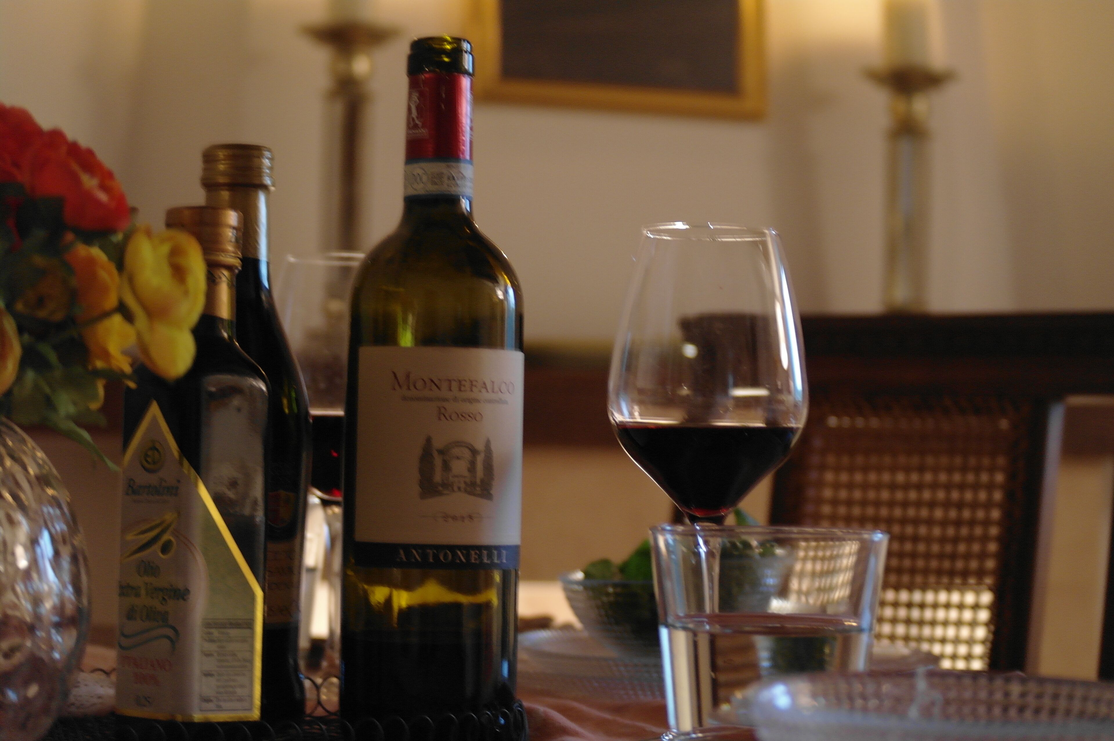 A table with a bottle of Montefalco Rosso wine, a glass of red wine, and other wine bottles.