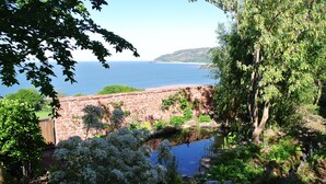 A garden with a pond, stone wall, and a view of the sea. - Stunning coastal home with panoramic sea views in Porlock Weir - 6 bed / 6 bath (Minehead)