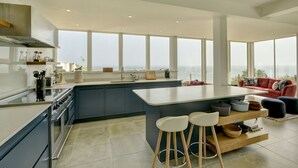 A modern kitchen with a large island, bar stools, and a view of the city. - Stunning coastal home with panoramic sea views in Porlock Weir - 6 bed / 6 bath (Minehead)