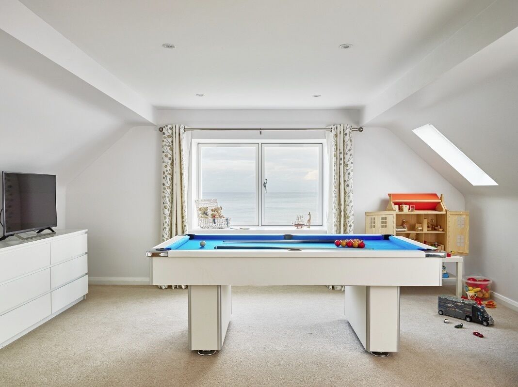 A room with a pool table, a television, a window with curtains, and a toy train set.