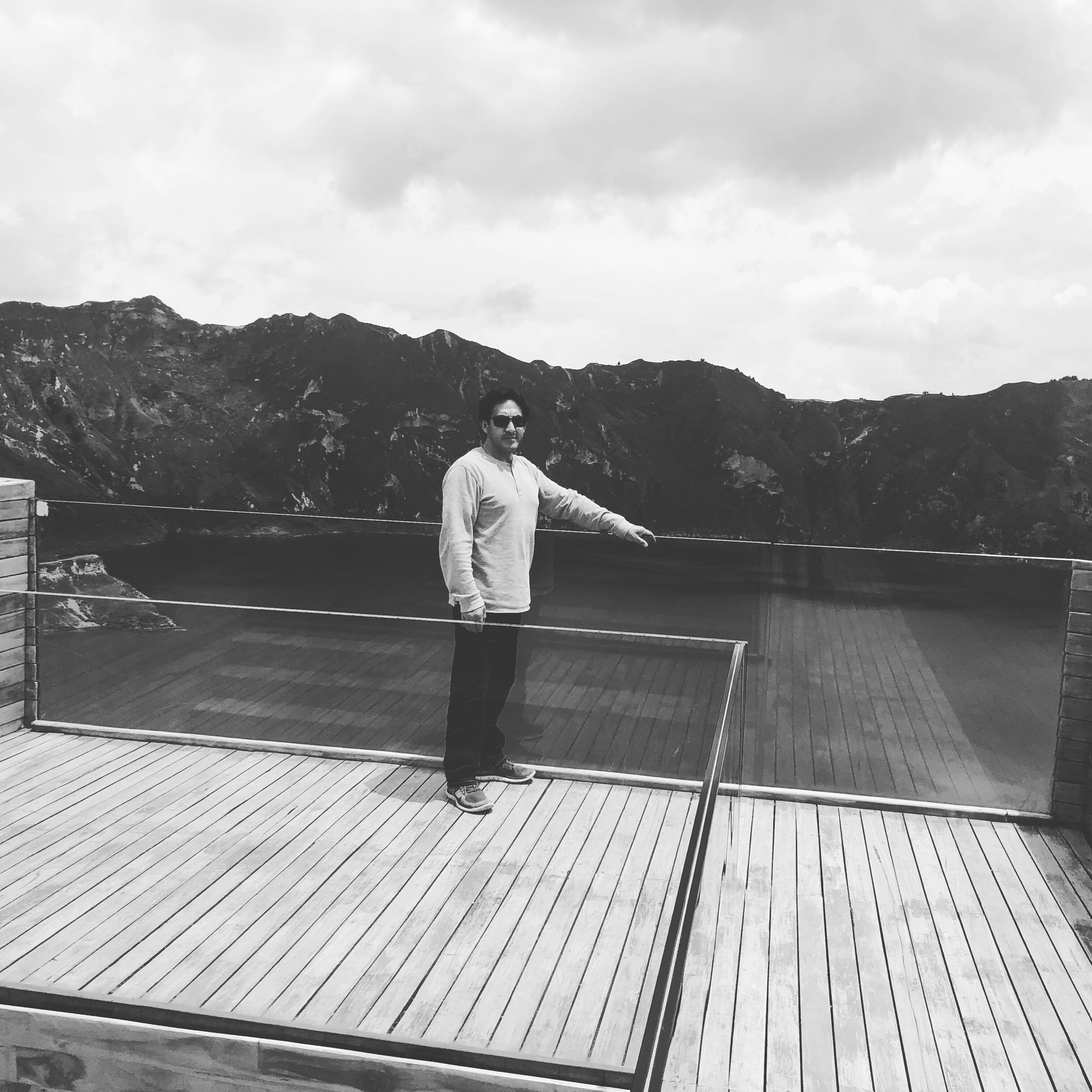 Una persona de pie en una terraza de madera con vistas a montañas al fondo.