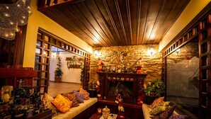 A cozy living room with a fireplace, wooden beams, and a stone wall. There are sofas with patterned cushions and a coffee table with decorative items. - Hostal Dulce Hogar (Latacunga)