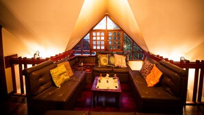 A cozy, triangular tent-style room with a sofa set and a table, featuring a large window and a hanging light fixture. - Hostal Dulce Hogar (Latacunga)