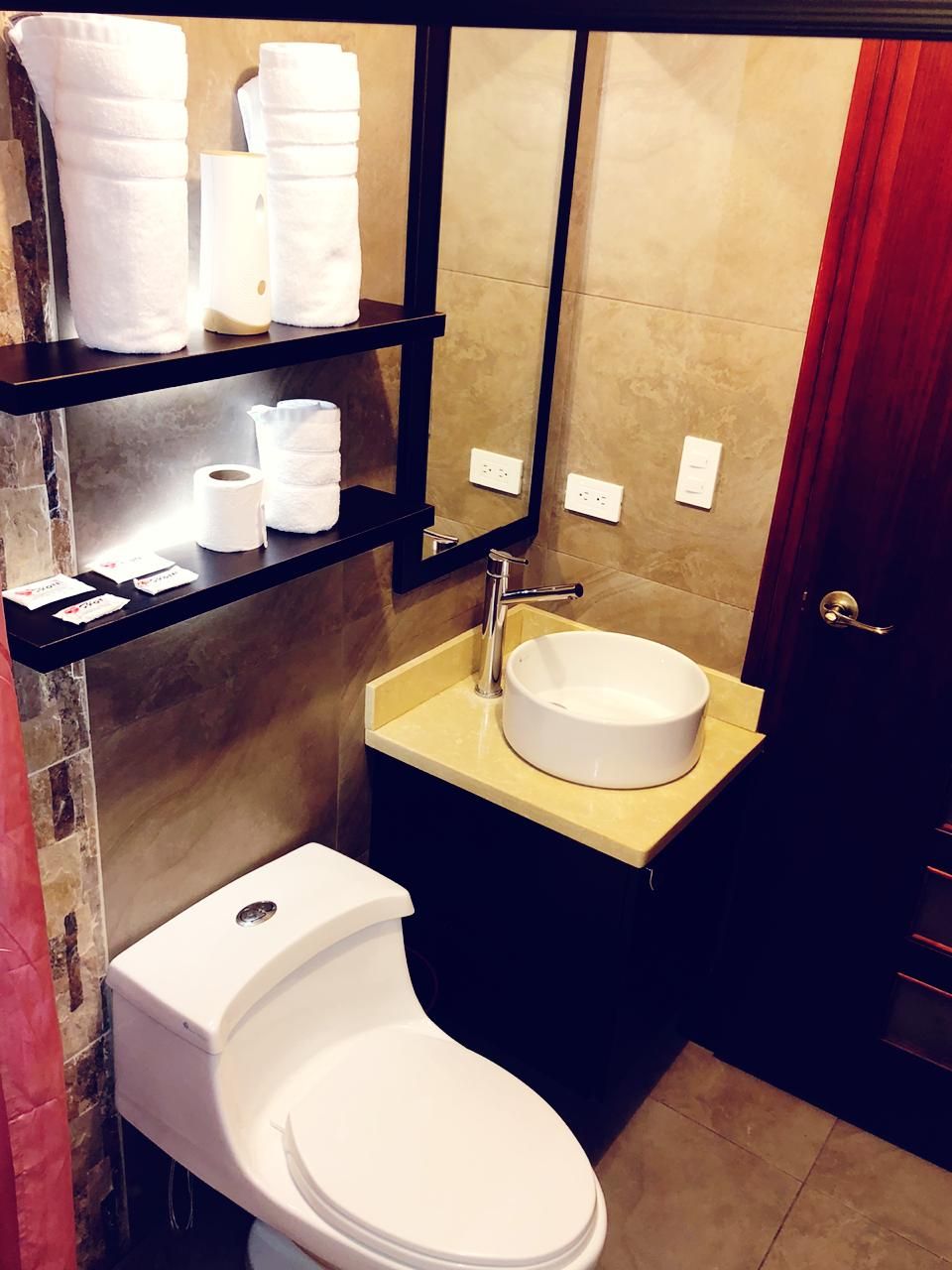 Un baño con inodoro, lavamanos y repisas con toallas y artículos de tocador.
