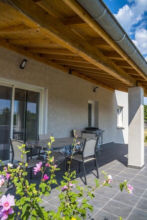 Un patio exterior con una pérgola de madera, una mesa con sillas y un ventanal corredero.