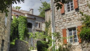Ein schmaler Steinweg führt zu einem rustikalen Steinhaus mit Efeu bewachsenen Mauern und hölzernen Fensterläden.