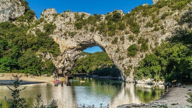 Ein natürlicher Felsbogen über einem Fluss, mit Kajakfahrern und einem Sandstrand.