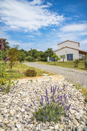 Una casa moderna con camino de grava, rodeada de follaje y plantas de lavanda.