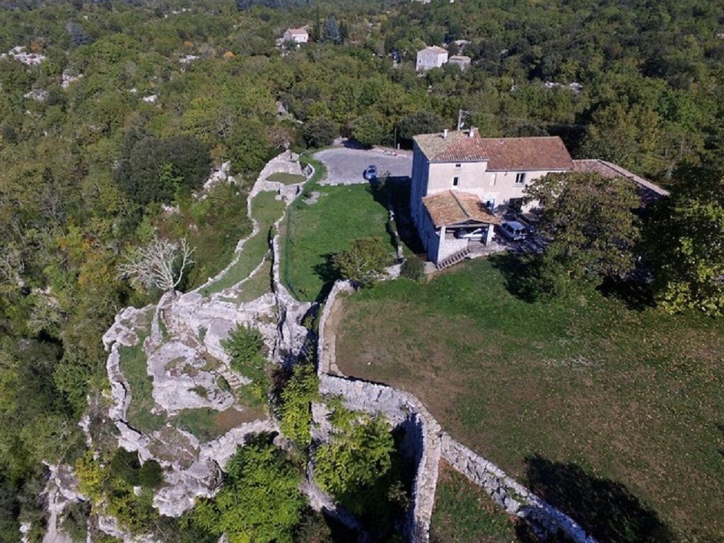 An aerial view of a property with a stone wall, a house with a tiled roof, and surrounding greenery.