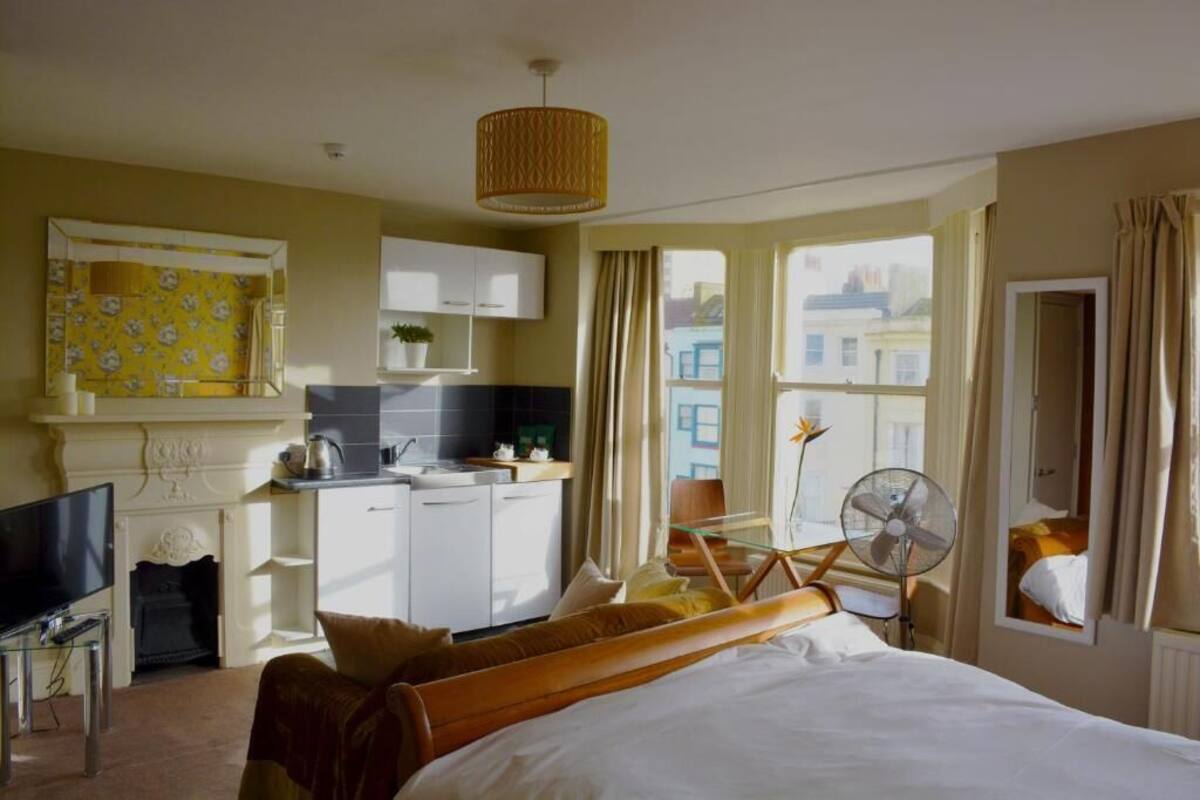 A hotel room with a bed, a television, a small kitchenette, and a view of the city.