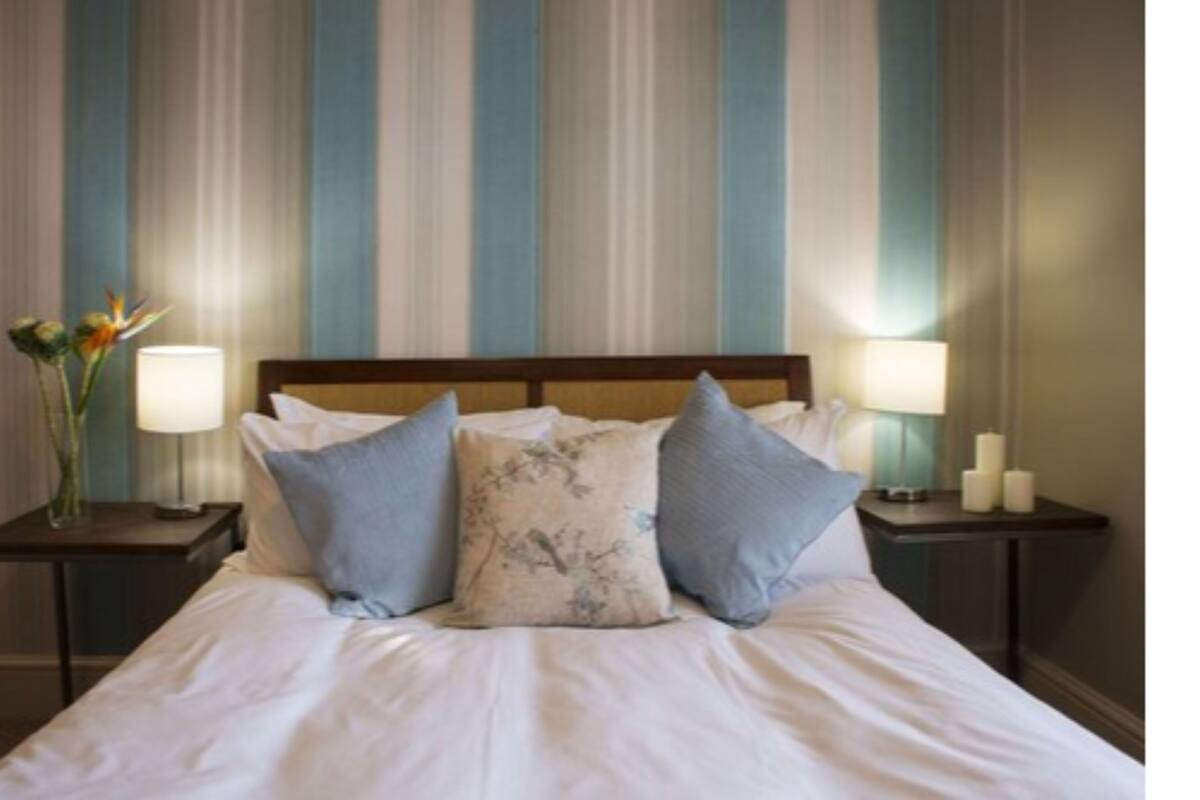 A neatly made bed with white linens and two pillows, flanked by two bedside tables with lamps and candles.