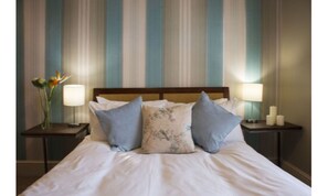 A neatly made bed with white linens and two pillows, flanked by two bedside tables with lamps and candles.