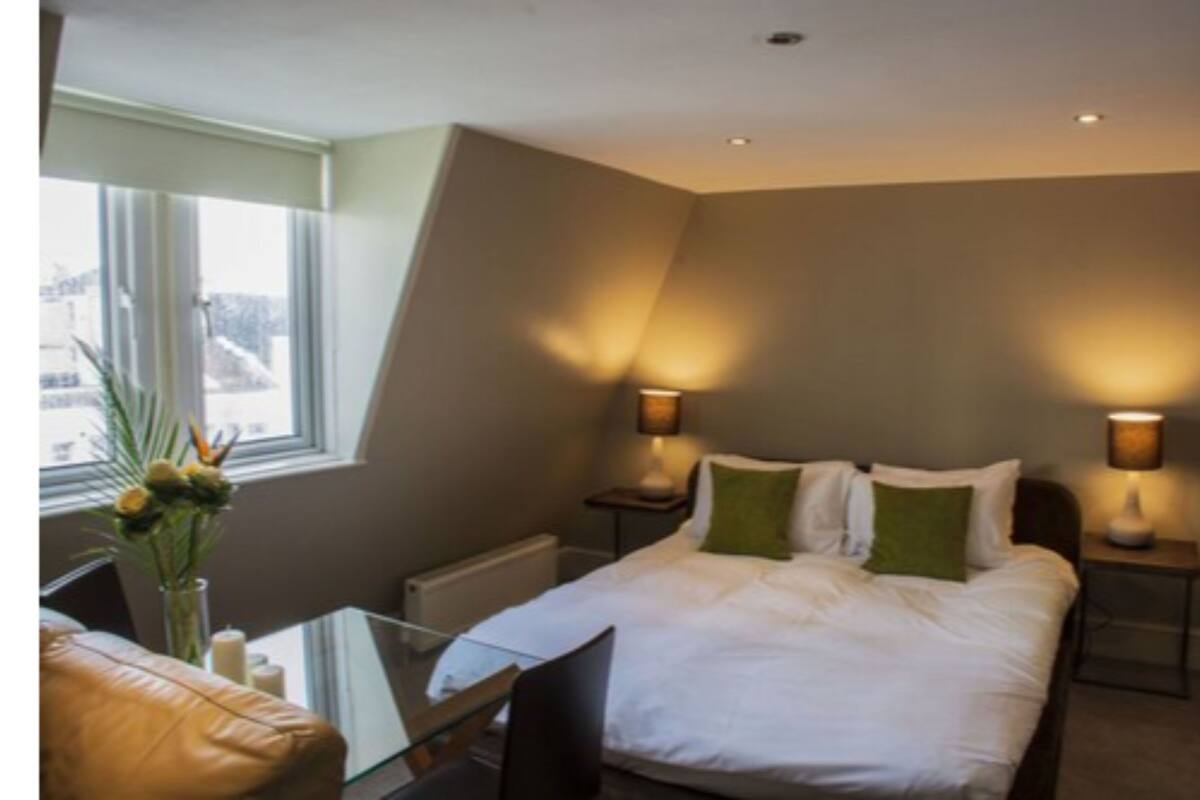 A bedroom with a bed, bedside lamps, a window, and a small table with a vase.