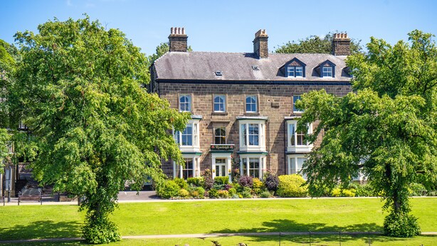 A large, historic building with a prominent entrance, surrounded by lush greenery and a calm water feature. - Roseleigh Guest House (Buxton)