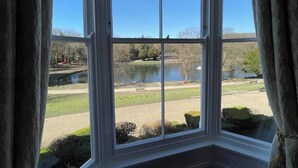 A view through a window with a clear sky, a body of water, and a park with grass and trees. - Roseleigh Guest House (Buxton)