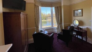 A hotel room with a large window, a flat-screen TV, a desk with a chair, and a mirror. - Roseleigh Guest House (Buxton)