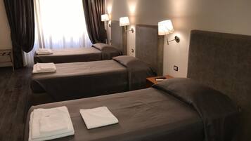 Habitación de hotel con tres camas, cada una con una toalla blanca, una mesita de noche con control remoto y lámparas de pared.