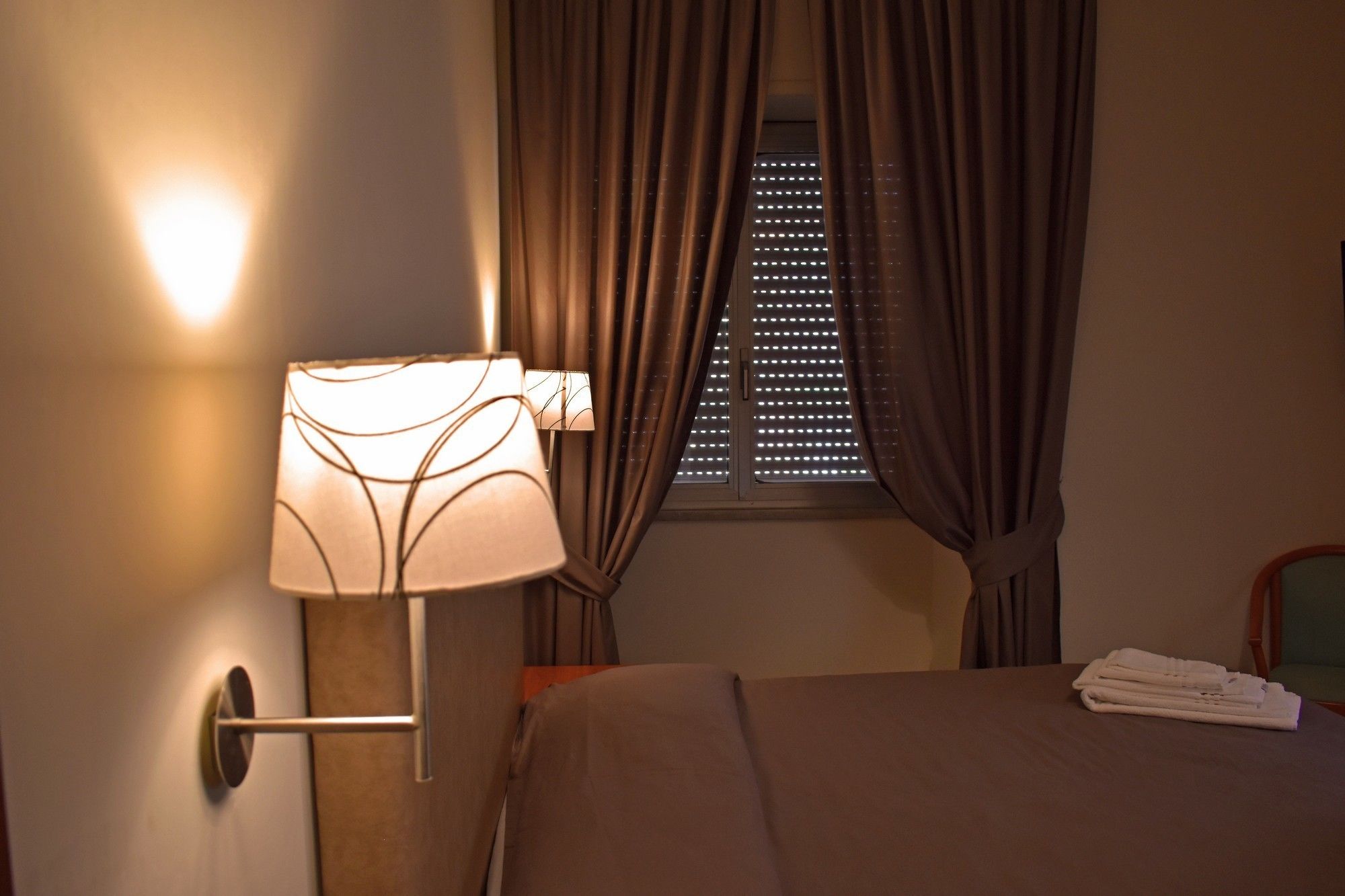 Een hotelkamer met een bed, een wandlamp en een raam met gordijnen.