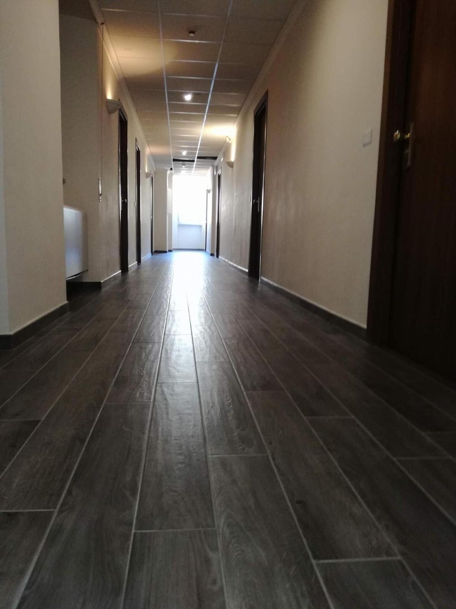 Un long couloir étroit, doté d’un plancher en bois foncé et de murs de couleur beige.