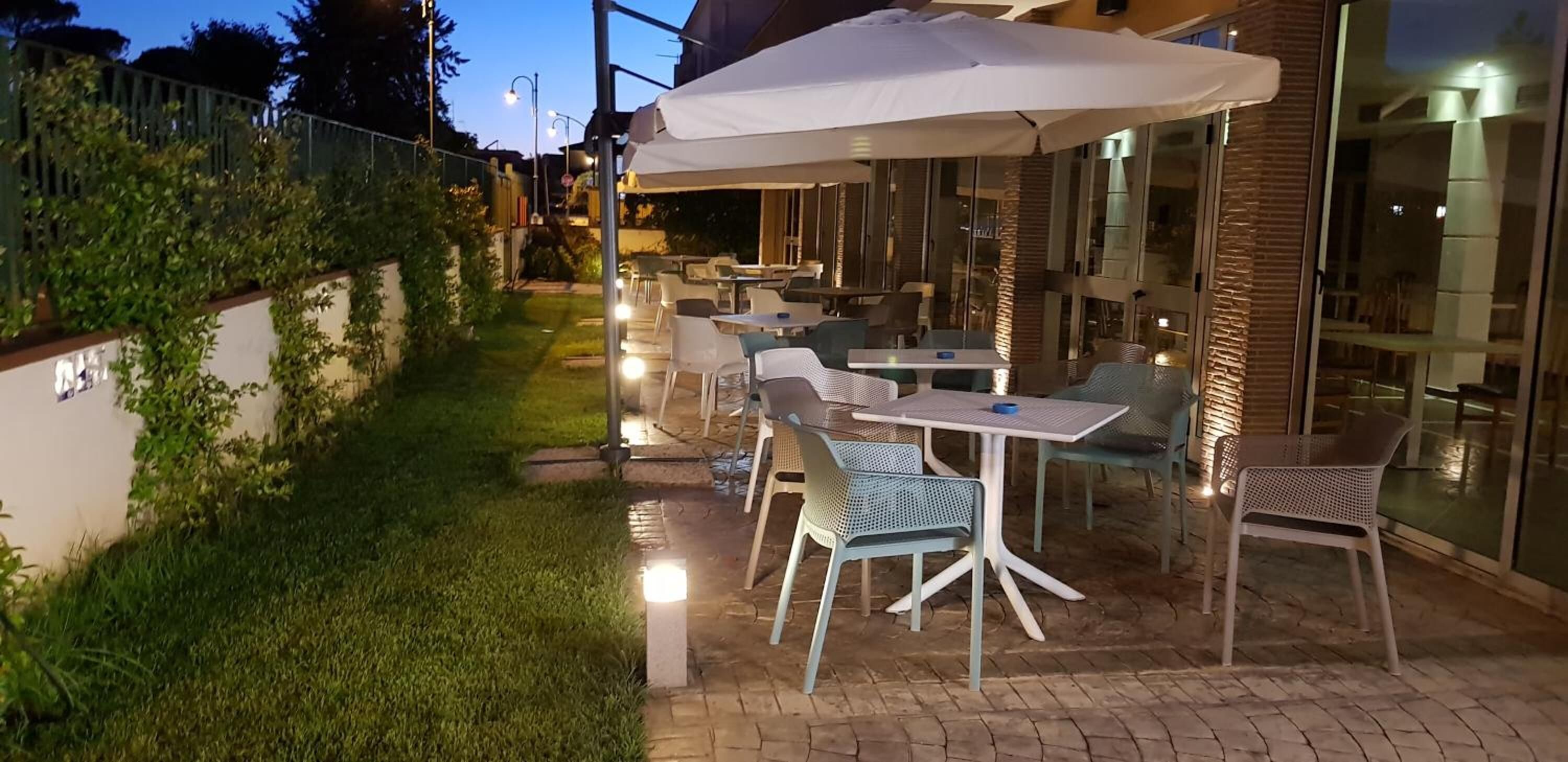 An outdoor patio with tables and chairs, a white umbrella, and a glass building in the background.