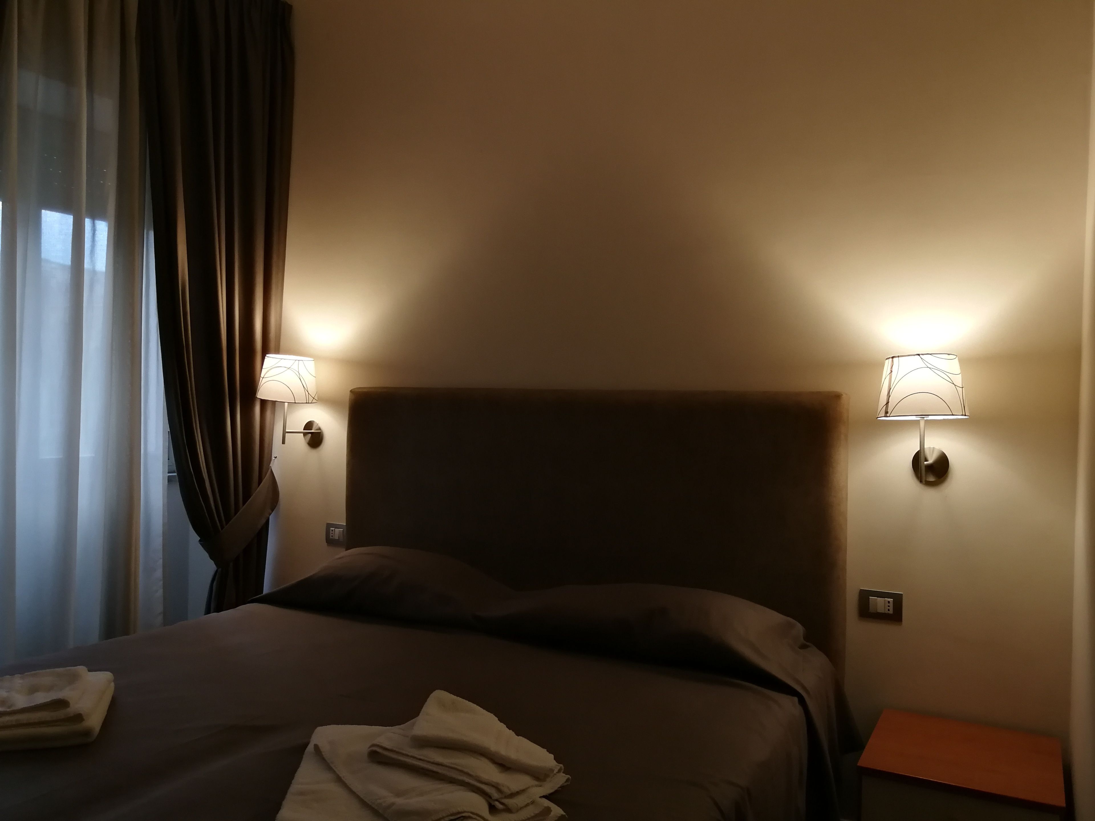 Habitación de hotel con una cama grande, dos lámparas de noche, una mesita de noche y una ventana con cortinas.