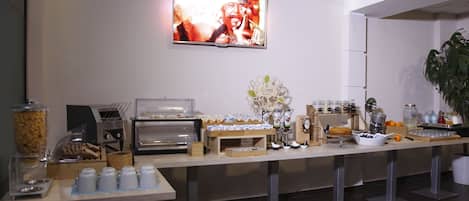 A buffet setup with a coffee station, food containers, and a television mounted on the wall.