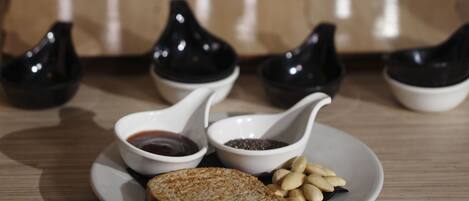 A table with three glass containers of tea, two small black cups, and a plate with toast and nuts.