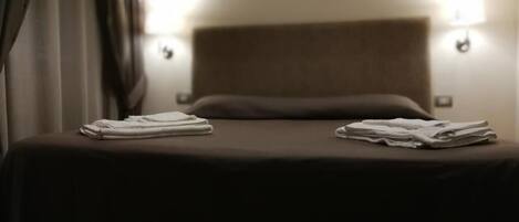 A hotel room with a bed, two wall-mounted lamps, and folded towels on the bed.