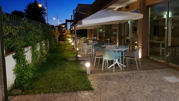 Un patio al aire libre con mesas y sillas, un sendero de césped y un edificio de vidrio al fondo.