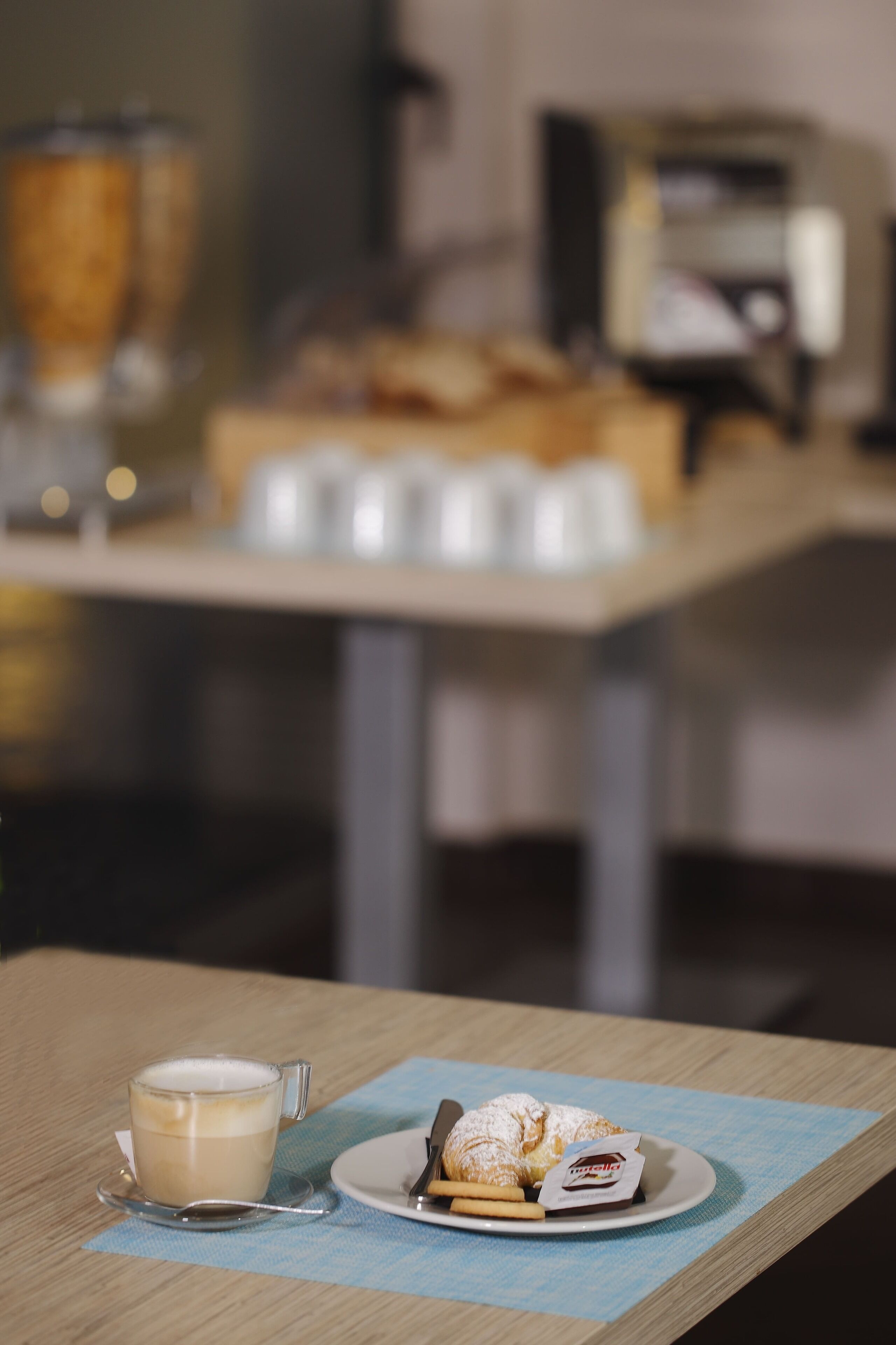 A table with a cup of coffee, a plate with a pastry, and a spoon.