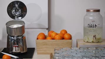 Een sapcentrifuge, een houten doos met sinaasappels, een waterdispenser en verschillende glazen op een tafel.