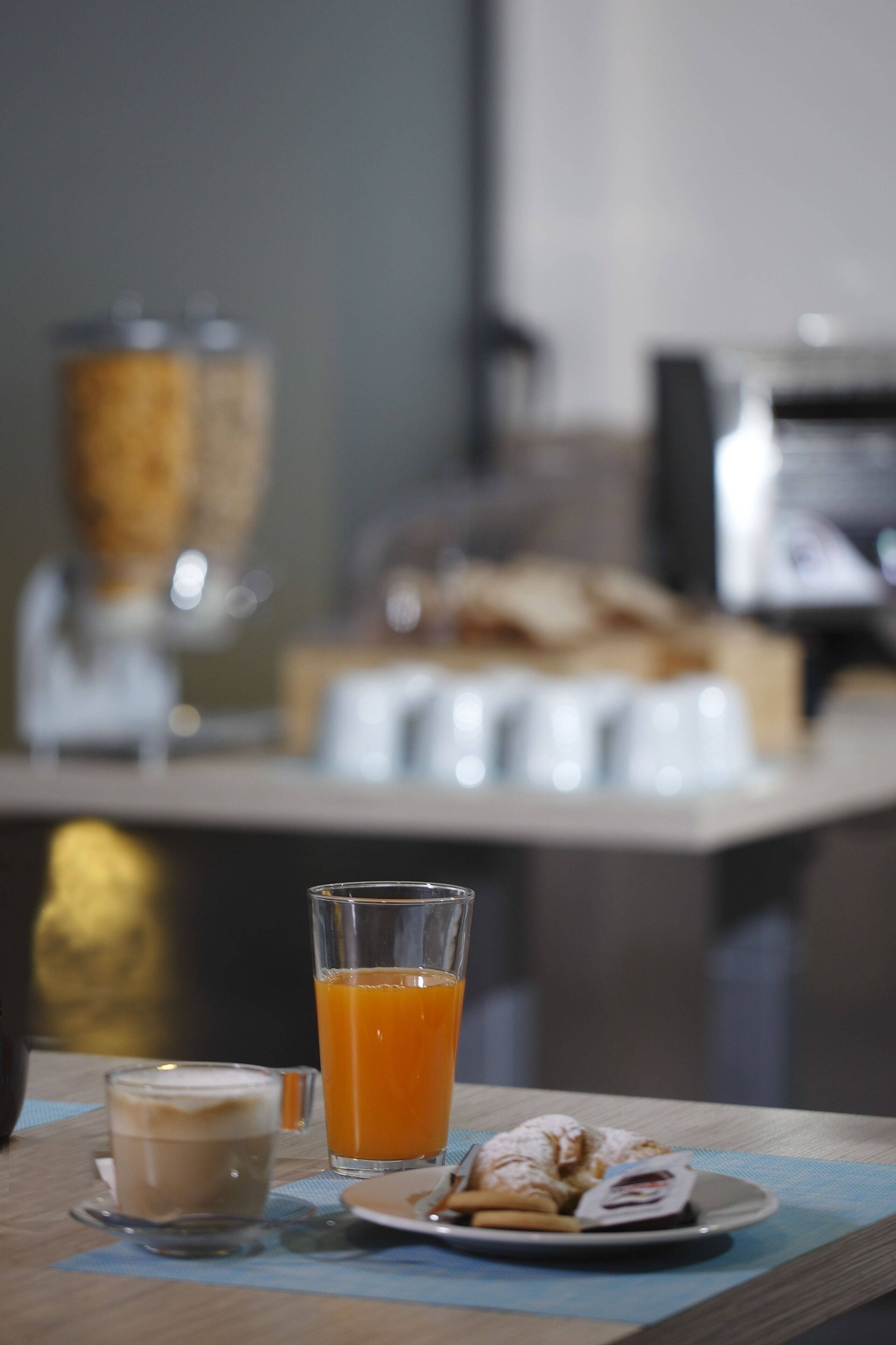 A breakfast table with a glass of orange juice, a cup of coffee, and a plate with croissants.