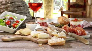 Diverse kazen, vleeswaren en een glas rode wijn op een houten tafel.