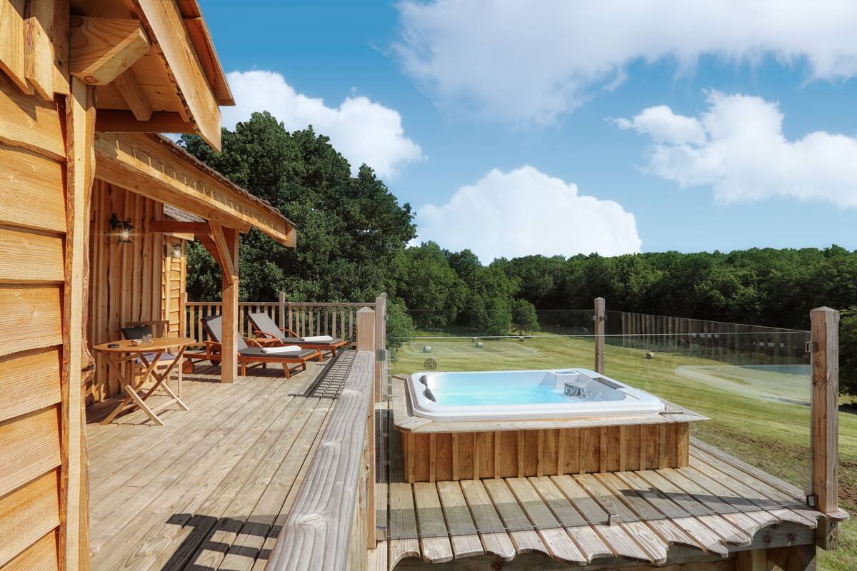 Een houten terras met een jacuzzi, lounge stoelen en een tafel.