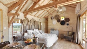 Een knus slaapkamer van een houten hut met een groot bed, een eettafel gedekt met borden en glazen, en uitzicht op de natuur.
