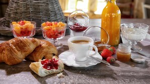 Een ontbijtje met croissants, fruit, koffie en een fles sinaasappelsap op een houten tafel.