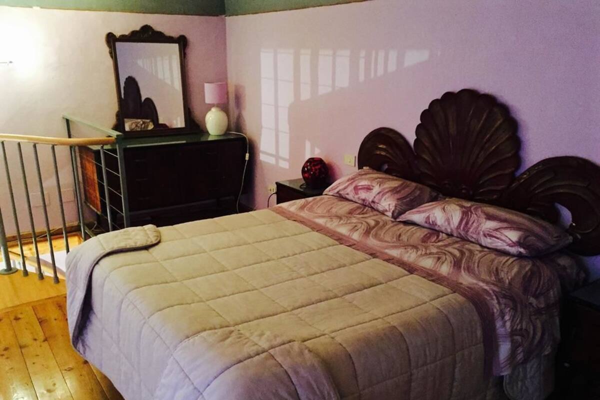 A bedroom with a bed, a nightstand, a dresser, a mirror, and a window.