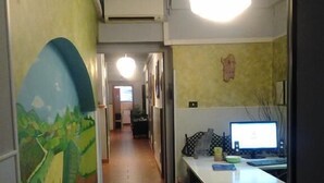 Ein Flur mit Wandgemälde links, einem Schreibtisch mit Computer rechts und einer Deckenleuchte.