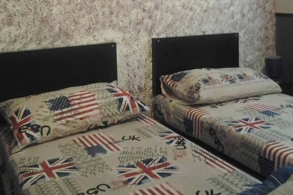 A room with two beds, each with a pillow featuring the UK flag. The walls have a floral wallpaper pattern.