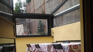 Eine Terrasse mit Esstischen, Blick ins Freie und einer Holzlattenverkleidung.