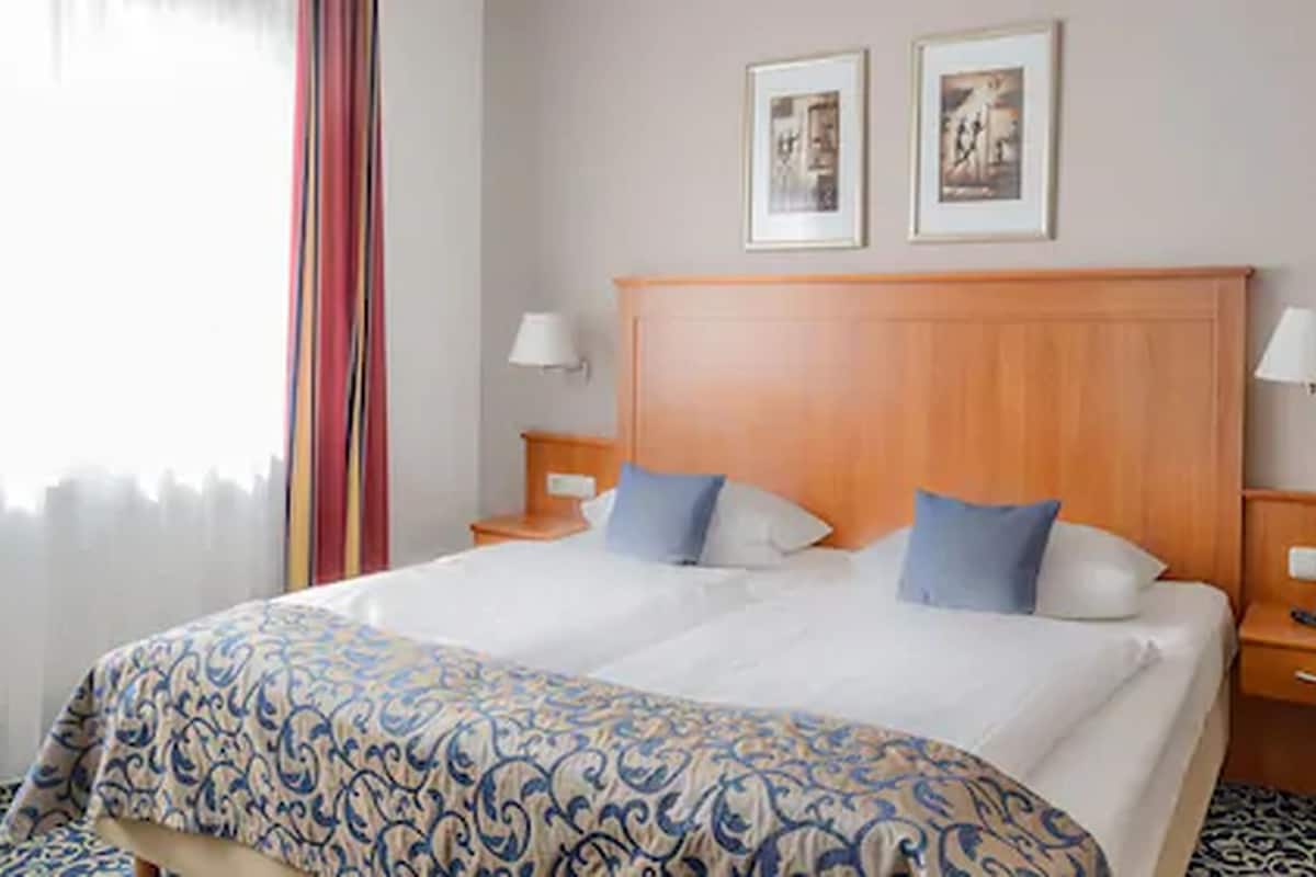 A double bed with a patterned bedspread, two pillows, a wooden headboard, bedside lamps, and two framed pictures on the wall.